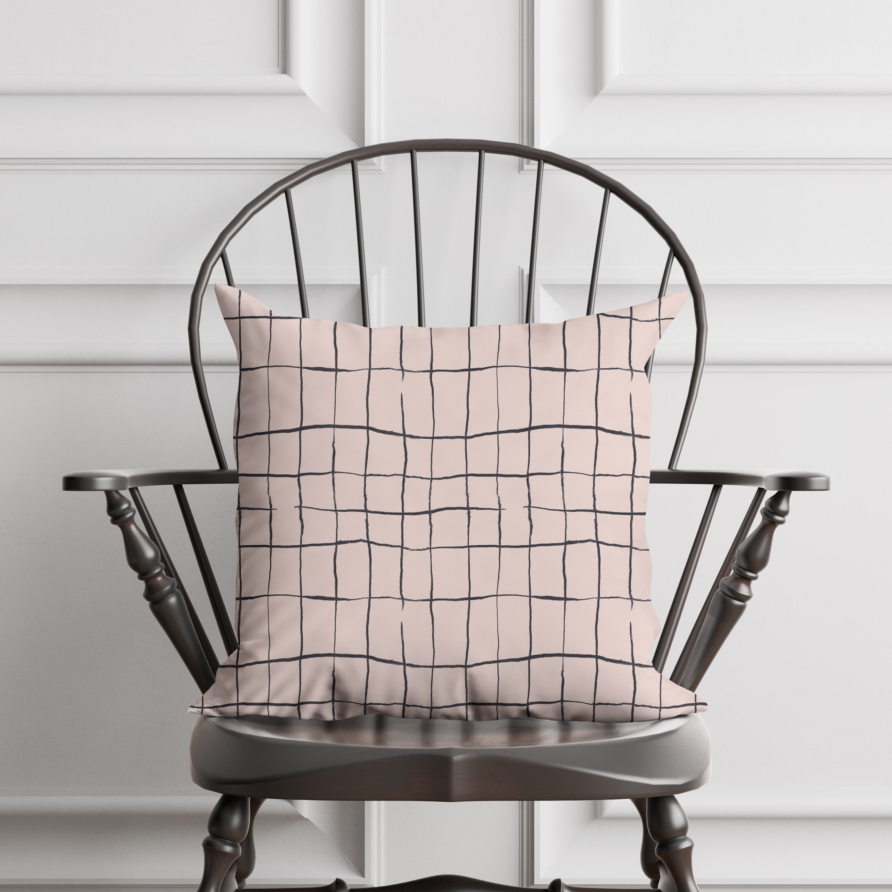 Decorative pillow with a broken grid pattern on a wooden chair against a white paneled wall.