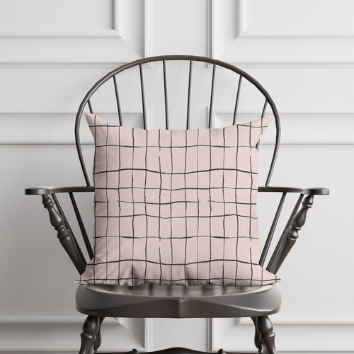 Decorative pillow with a broken grid pattern on a wooden chair against a white paneled wall.