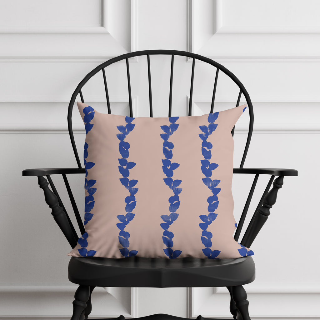 Beige pillow with blue leaf pattern on a black chair against a white paneled wall.